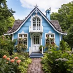 a blue house with white trim surrounded by greenery and flowers in the front yard