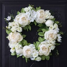 a wreath with white flowers and greenery on a black door frame in front of a brick wall