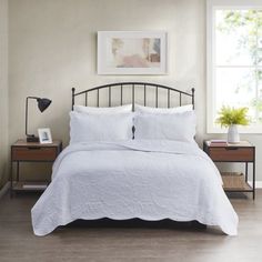 a bed with white linens and pillows in a small room next to a window