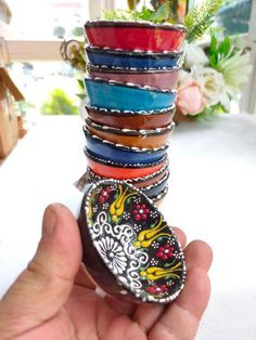 a hand holding a stack of bracelets with different designs on them in front of a window