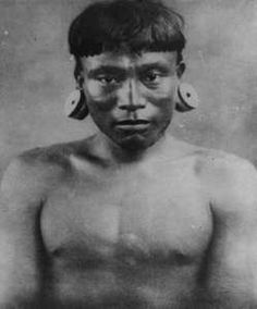 an old black and white photo of a man with large earrings on his head, looking at the camera