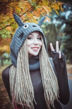 a woman with long blonde dreadlocks wearing a knitted hat and making the peace sign