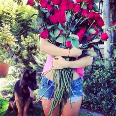 a woman is holding roses in her arms with a dog sitting next to her on the grass