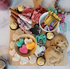 a wooden cutting board topped with lots of cookies and other treats on top of a table