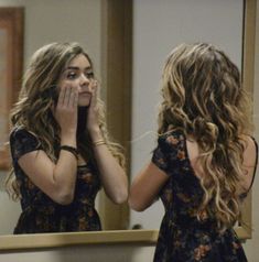 a woman standing in front of a mirror looking at her face and covering her eyes