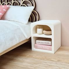 a small white shelf with books on it next to a bed and pillows in a bedroom