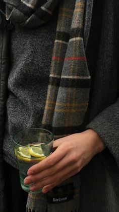 a woman is holding a glass with lemons and limeade in it while wearing a scarf