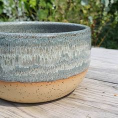 a large bowl sitting on top of a wooden table next to trees and bushes in the background