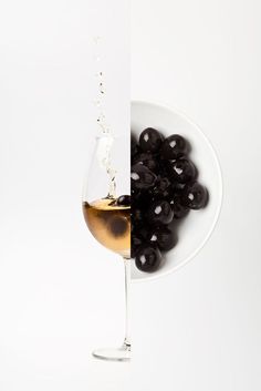 a white plate topped with black olives next to a wine glass filled with liquid