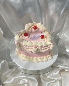 a pink and white birthday cake with cherries on top sitting on a glass plate