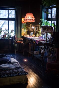 a bedroom with a bed, desk and lamp in it's dark room next to two large windows