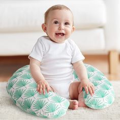 a baby sitting on the floor with a green and white pillow in front of it