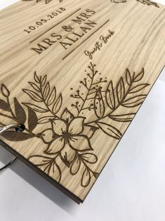 a wooden wedding guest book with flowers and leaves engraved on the front, in black ink