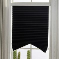 the window is covered with black blinds in front of white drapes and green plants