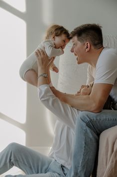 a man holding a baby up to his face while sitting on a couch with another person