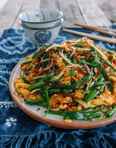 a white plate topped with stir fried vegetables and veggies next to chopsticks