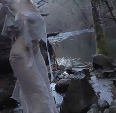 a woman in white dress standing on rocks near water