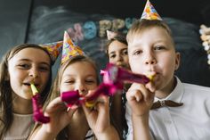 three young children wearing party hats and holding streamers in front of their mouths,