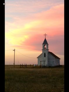 an old church sits in the middle of a grassy field with a sunset behind it