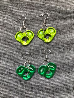 four pairs of green and white earrings on top of a gray cloth covered tablecloth