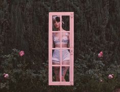 a woman is standing in front of a mirror with flowers around her and bushes behind her