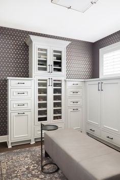 a room with white cabinets, drawers and a bench in front of a window that has blind shades on it