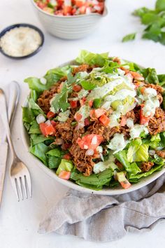 a salad with meat, lettuce and tomatoes in a bowl next to a fork