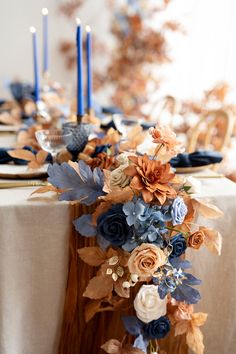 the table is set with blue and orange flowers, candles and napkins on it