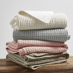 folded blankets stacked on top of each other in various colors and patterns, sitting on a wooden surface