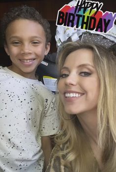 a woman standing next to a boy wearing a birthday hat