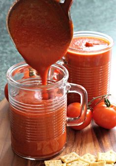 a wooden cutting board topped with two jars filled with sauce and crackers next to tomatoes