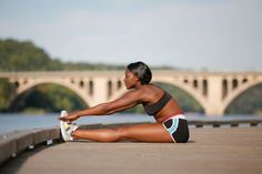 a woman stretching her legs on the side of a bridge with a river in the background