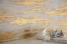 a white counter top topped with bowls and saucers next to a wall covered in gold tiles