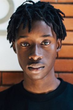 a man with dreadlocks standing in front of a brick wall and looking at the camera