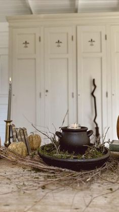 a table with candles, books and other items on it in a room filled with white cupboards