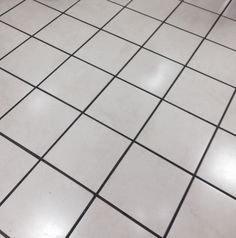 a white tiled floor with black grouting on the top and bottom tiles, in a bathroom