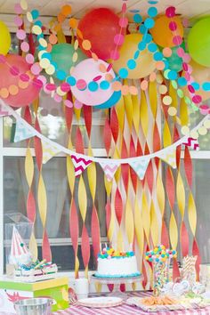 a birthday party with balloons and streamers hanging from the ceiling, cake on table