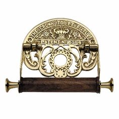 a brass plated toilet paper holder with wooden handle and ornate design on the front