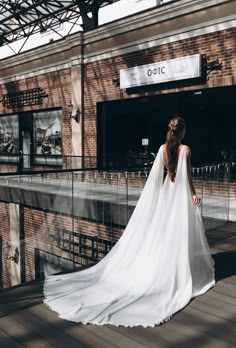 a woman in a white wedding dress is standing on a wooden deck outside the building