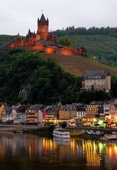 an old castle sits on top of a hill next to a river with boats in it