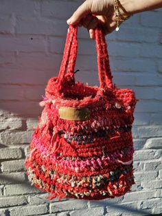 a hand holding a red bag with multicolored crocheted material on it