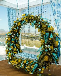 a blue and yellow wreath with flowers hanging from it's sides in front of a window