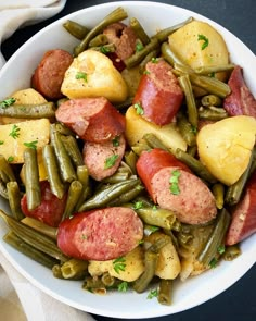 a white bowl filled with potatoes, green beans and sausage