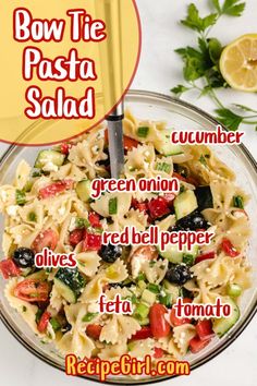 a bowl filled with pasta and vegetables on top of a white table next to lemon wedges