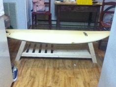 a white surfboard sitting on top of a wooden table in a room with chairs