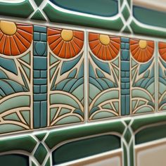 an art deco tile design on the side of a building with orange and blue flowers