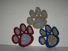 three different colored dog paw prints on a white wall, one with gold and silver glitter