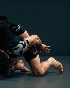 two men wrestling in a black and white ring with their hands on each other's knees