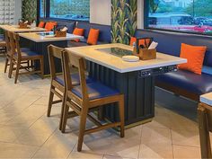 an empty restaurant with blue booths and orange pillows on the seats, looking out onto the street