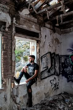 a man sitting on the window sill of an abandoned building with graffiti all over it